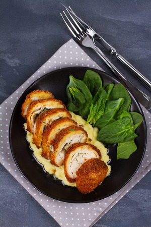 Chicken Kiev on mashed potato with spinach. Breaded chicken breast stuffed with herbs and butter on black plate. View from above, top studio shotの写真素材