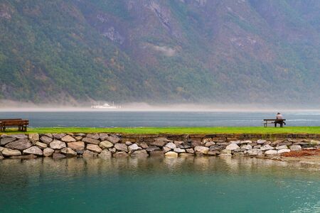 View at fjord and lake. Lonely man is sitting on the promenade. Sea and mountains landscape, Norwayの写真素材