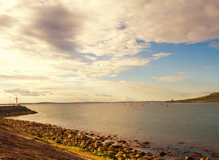 Photo of a beautiful scenic sea landscape. Yachts in sea, view on Howth Harbour Lighthouse, Howth Peninsula, county Dublin, Ireland. Lightly tonedの写真素材