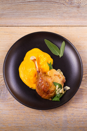 Roast duck leg with mashed pumpkin (butternut squash), sage and garlic on plate, closeup. Horizontal view from above, top shotの写真素材