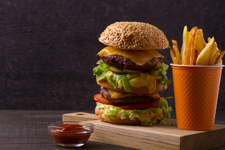 Homemade triple decker burger and fries on dark wooden background, horizontalの写真素材
