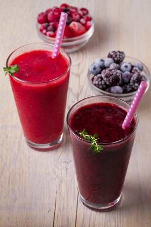 Frozen summer berries smoothie: blueberries, strawberries, raspberries, cranberries, currants and blackberries on wooden background, verticalの写真素材