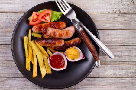 Grilled sausages with fries. Sausages with potatoes and vegetables. View from above, top, horizontalの写真素材