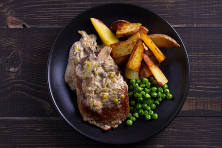 Beef steak with mushroom cream sauce, potato wedges  and green peas. View from above, top の写真素材