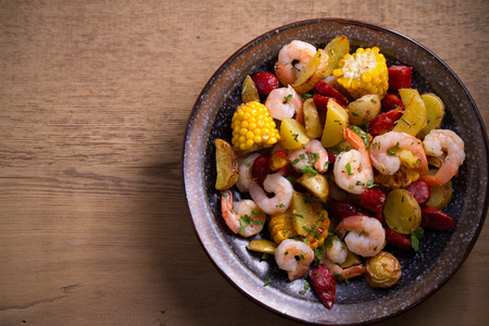 Shrimp boil. Shrimps, smoked sausages, potatoes and corn in bowl on wooden table. overhead, horizontalの写真素材