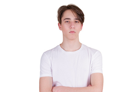 Confident serious young man keeping arms crossed. Handsome teen boy looking at camera. Portrait of teenager in white T-shirt, isolated on white backgroundの写真素材