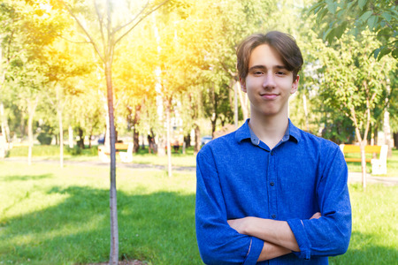 Young man looking at camera, smiling. Portrait of teen boy in blue jeans shirt, keeping arms...