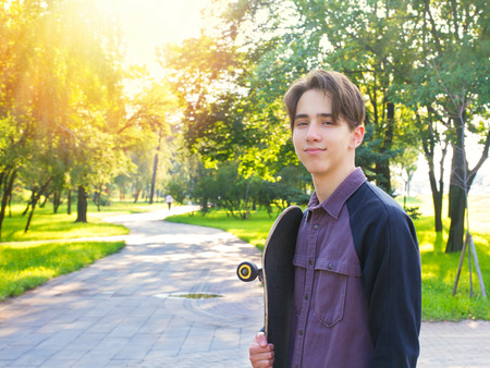 Young man standing with skateboard in hands in city park. Teen boy skaterの写真素材