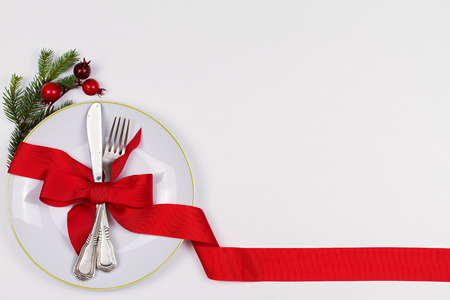 Christmas composition with plate, cutlery, pine branches, ribbon and red berries on white table. Winter holidays and festive background. Christmas eve dinner, New Year food lunch.  top viewの写真素材