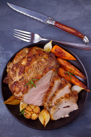 Baked ham with vegetables: carrots, onions, garlic and herbs. View from above, top studio shotの写真素材