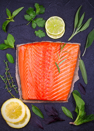 Fresh uncooked salmon fish with lemon, lime and herbs on black background. Flatlay food setting. View from above, top の写真素材