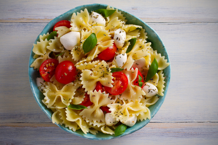 Caprese Pasta Salad. Pasta with mozzarella cheese, tomatoes and basil in bowl on wooden table. overhead, horizontalの写真素材