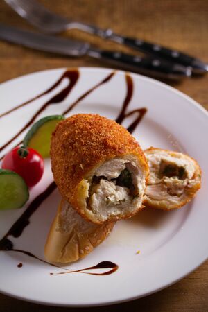 Chicken Kiev and vegetables on white plate, wooden background. Breaded chicken breast stuffed with...