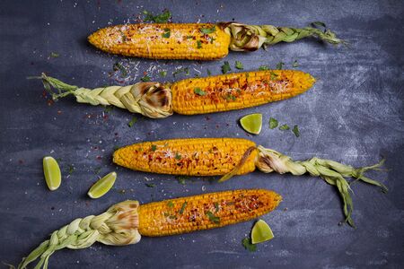 Top view of grilled sweet corn cob with parmesan cheese, paprika, salt, cilantro and lime