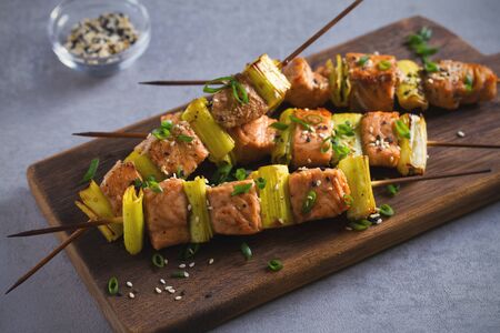 Skewered salmon teriyaki with leeks, sprinkled with sesame seeds on serving board. Horizontal imageの写真素材