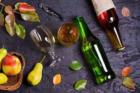 Bottles and glass of apple and pear cider with fruits and leaves on black background. Overhead horizontal imageの写真素材