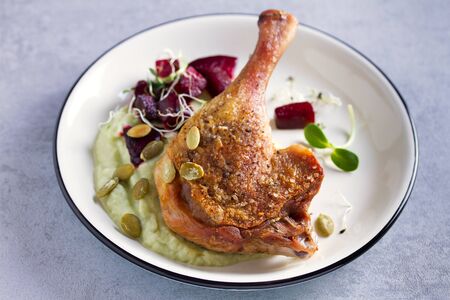 Roast duck leg with mashed green vegetables, beetroot, and pumpkin seeds on light gray backgroundの写真素材