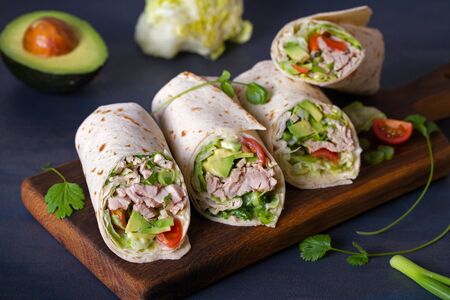 Turkey wraps with avocado, tomatoes and iceberg lettuce on chopping board. Tortilla, burritos, sandwiches, twisted rollsの写真素材