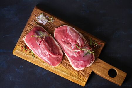 Raw fresh meat, duck breast fillet on wood chopping board with rosemary and seasons. Flat layの写真素材