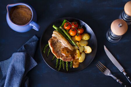 Roast pork chop with pepper sauce, asparagus, potatoes and tomatoes. View from above, top viewの写真素材