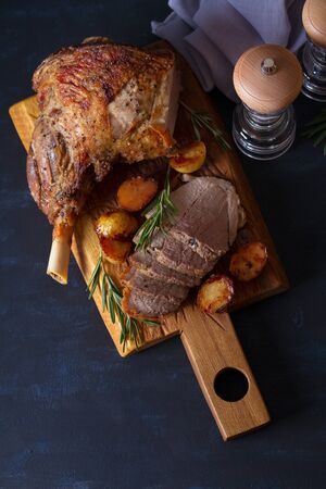 Roast leg of lamb with potatoes and rosemary on dark background.の写真素材