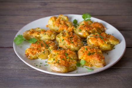 Smashed new baby potatoes with garlic butter and cheese on wooden background close up. Clean eatingの写真素材