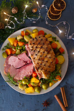 Roasted sliced ham with vegetables. Christmas decorations. New Year dinner table. View from above, top studio shotの写真素材