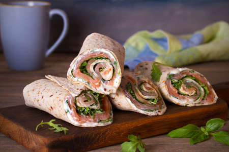 Salmon and cream cheese wraps. Rolls with smoked salmon, basil and rocket salad. Burrito on serving boardの写真素材