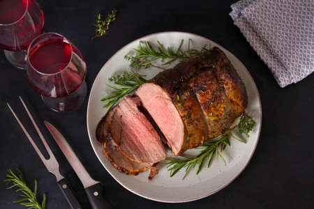 Roasted beef with herbs and red wine on dark background. View from above, top studio shotの写真素材