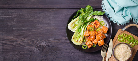 Delicious salmon with salad, rice and sesame seeds on black plate and black wooden background. View from above with copy spaceの写真素材