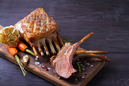 Roasted rack of lamb. Lamb chops with vegetables on serving wooden boardの写真素材