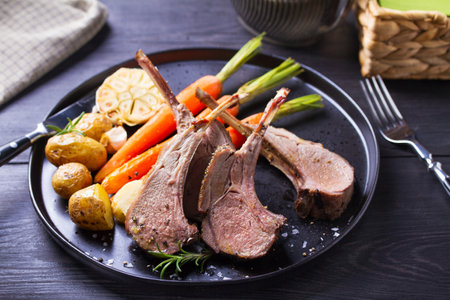 Lamb chops with carrots and potatoes, black background. Roasted rack of lambの写真素材