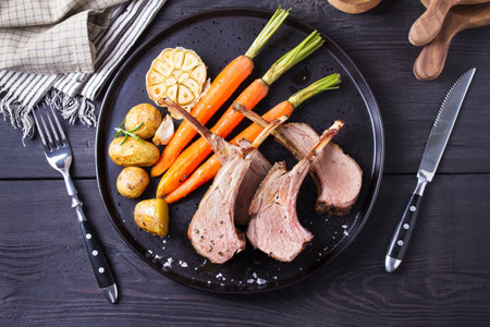 Lamb chops with carrots and potatoes, black background. Roasted rack of lamb. High angle viewの写真素材