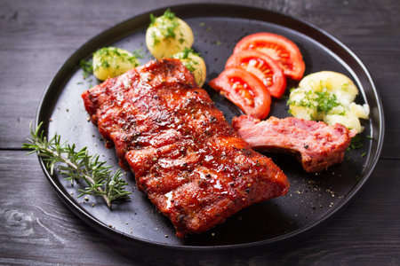 Barbecue grilled pork ribs with boiled potatoes and fresh vegetables, black backgroundの写真素材