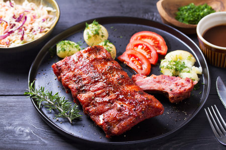 Barbecue grilled pork ribs with boiled potatoes and fresh vegetables, black backgroundの写真素材