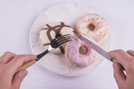 Hands with fork and knife on strawberry and chocolate donutsの写真素材