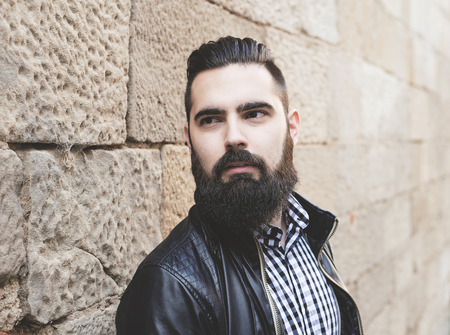 Closeup of modern young bearded man leaning against the wall. Hipster