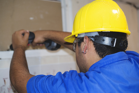 Construction worker with yellow helmet using an electric screwdriver