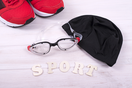 Red sneakers, hat and goggles for swimming pool laying near sport letters. Horizontal studio shotの写真素材