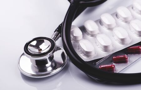 Pills and metal stethoscope on white surface. Horizontal studio shot. の写真素材