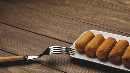 Croquettes on white tray next to a fork on brown wooden table. Horizontal shoot.の写真素材