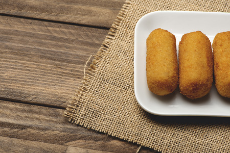 Croquettes in a white tray on the corner of a cloth and brown wooden table. View from above. Appetizerの写真素材