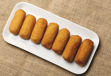 Croquettes in a white tray on cloth and brown wooden table. View from above.  