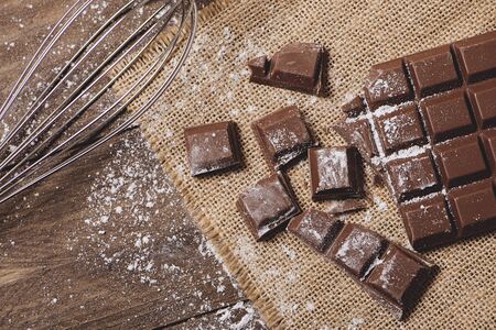 Tablet and chocolate pieces with icing sugar next to cookware. Horizontal shoot.