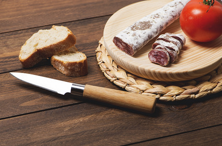 Fuet cut with a knife and a tomato on a wooden table. Horizontal shoot.の写真素材