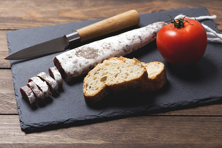 Fuet and a knife next to a tomato on a slate plate. Spanish sausage. Horizontal shoot.の写真素材