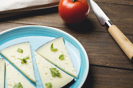 Blue dish with cheese on rustic brown wooden table next to a knife and a tomato. Horizontal shoot.の写真素材
