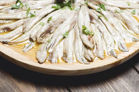 Close-up of anchovies with olive oil and vinegar on a wooden plate on a brown wooden table. Healthy food.の写真素材