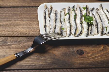 Plate of anchovies next to a fork on brown wooden table.の写真素材