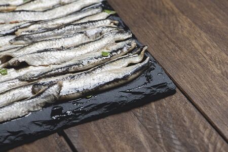 Anchovies with olive oil and vinegar on a plate of slate on wooden table. Food. Horizontal shoot.の写真素材